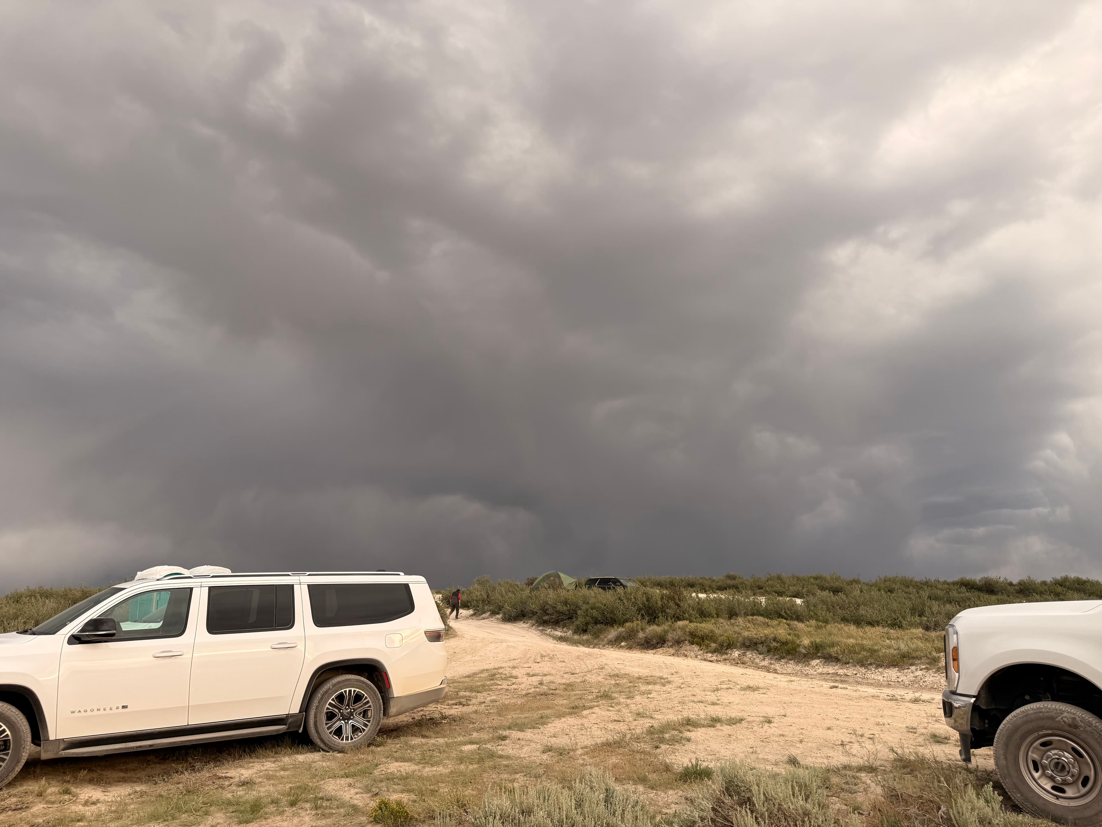 Stormy skies over the dig site with parked vehicles and tents.