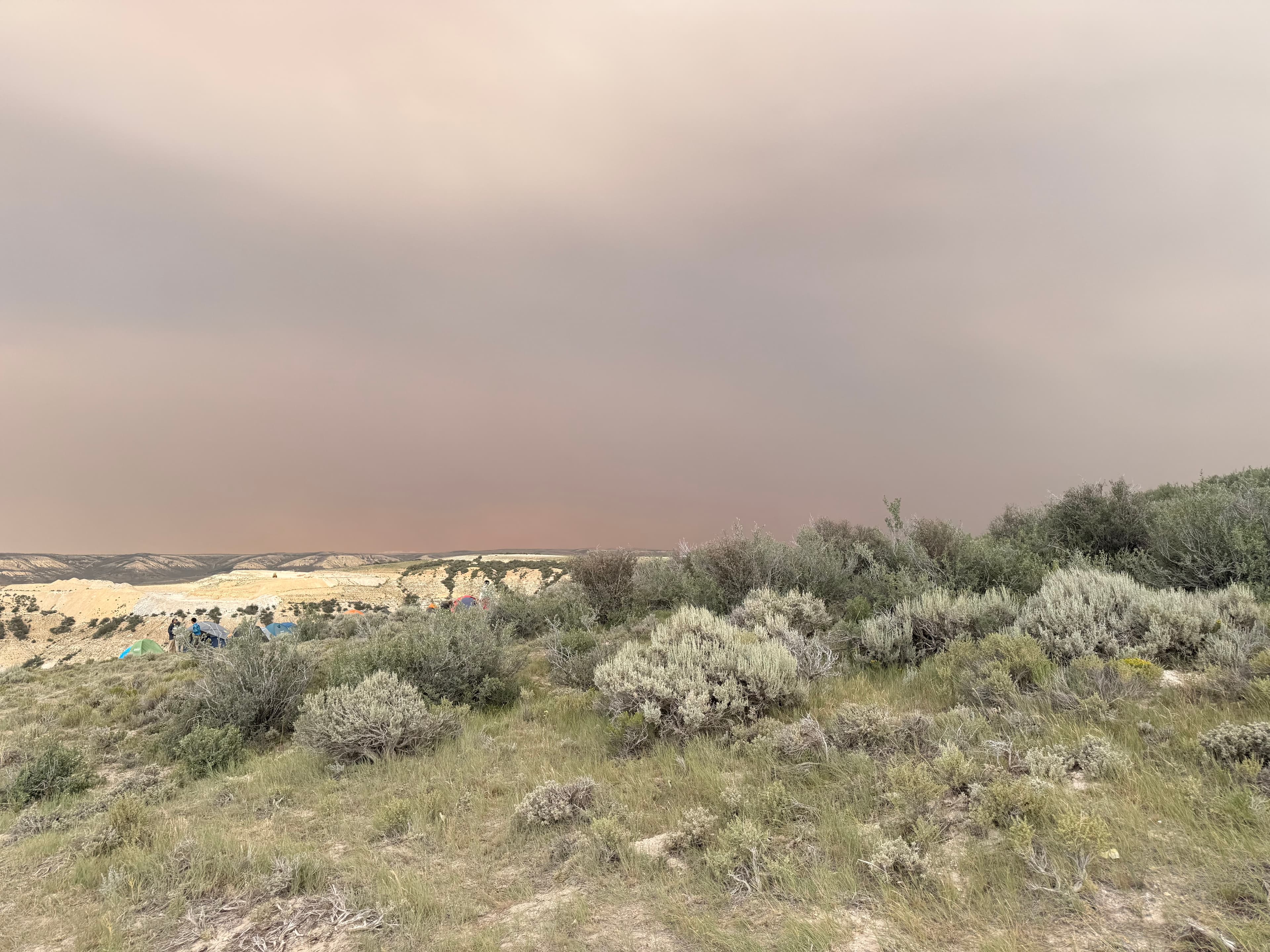 Camp tents and people in a dusty landscape under a hazy sky.