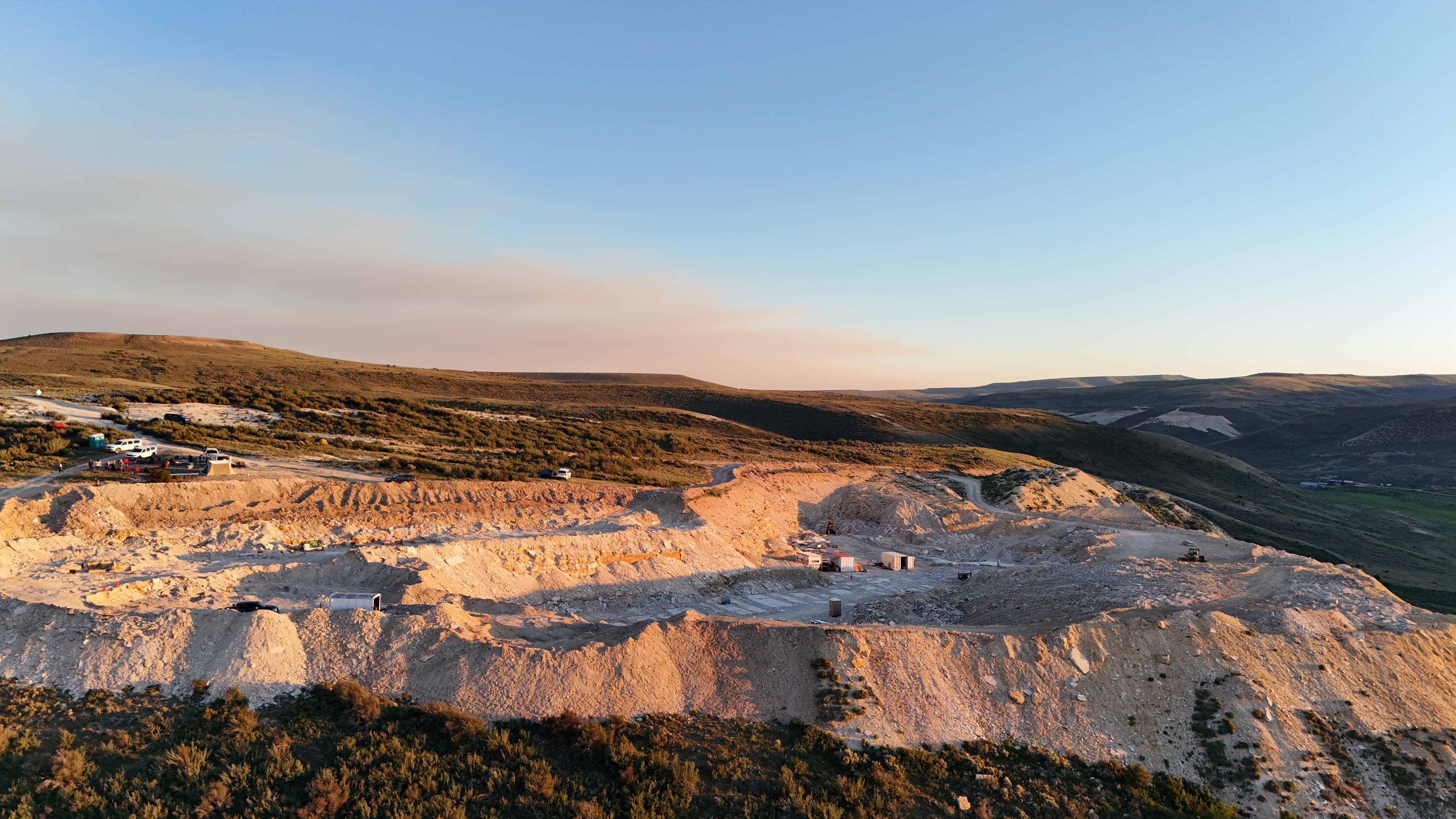 Loader and tents at the quarry with distant hills at sunset.