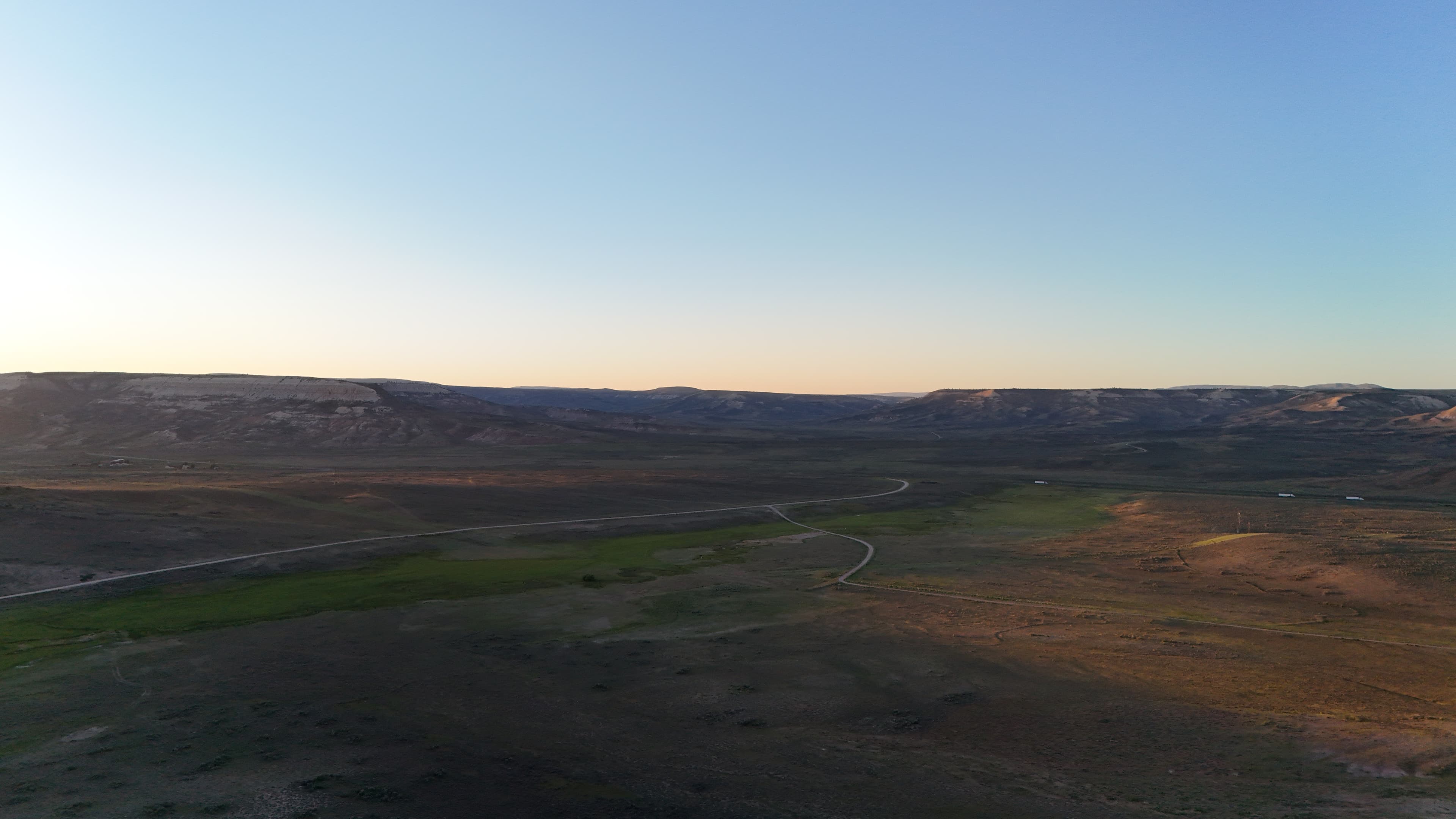 Wide valley with rolling hills under a clear sky at sunset.