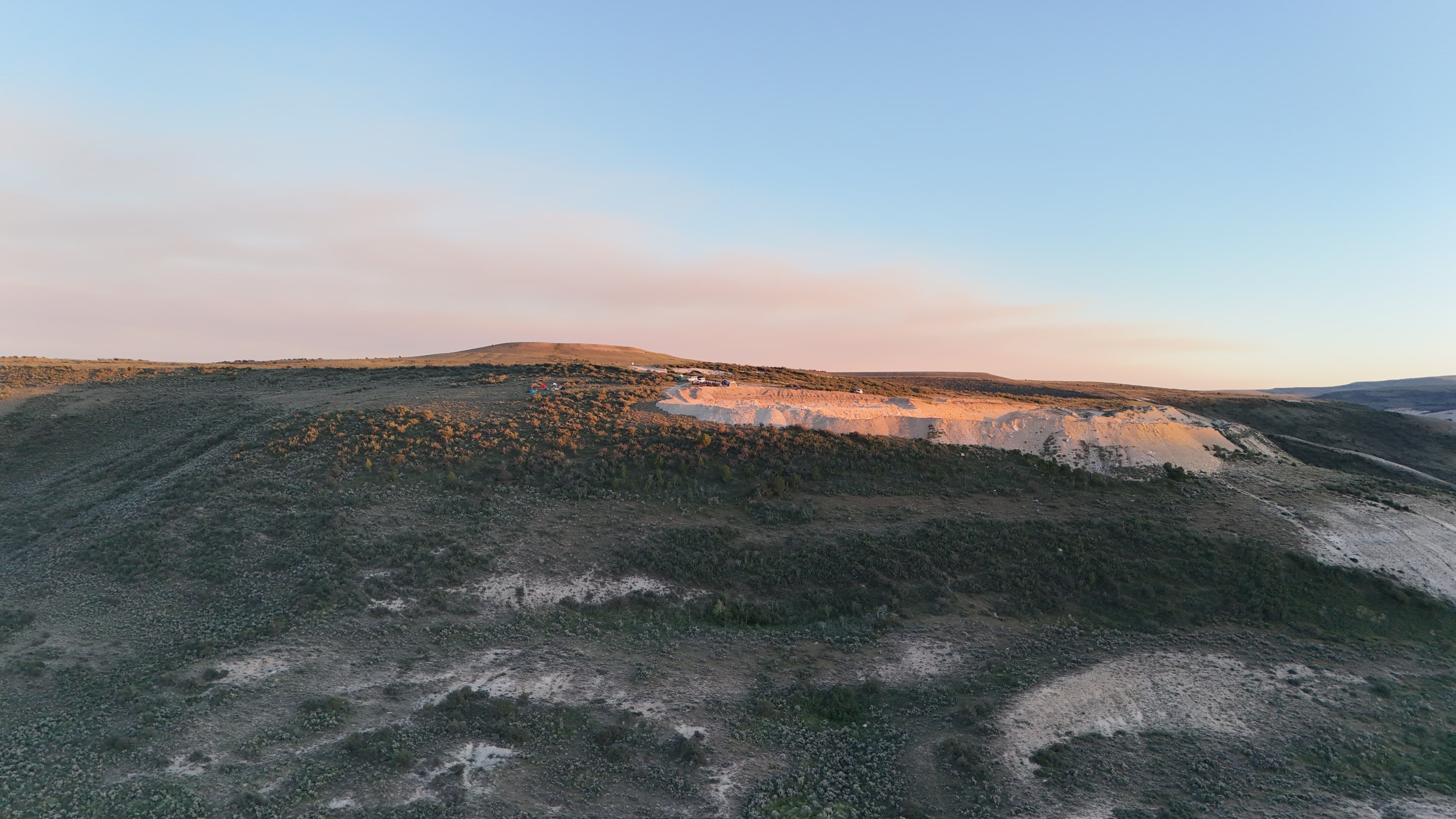 Quarry site with tents and trucks under a pastel sky.