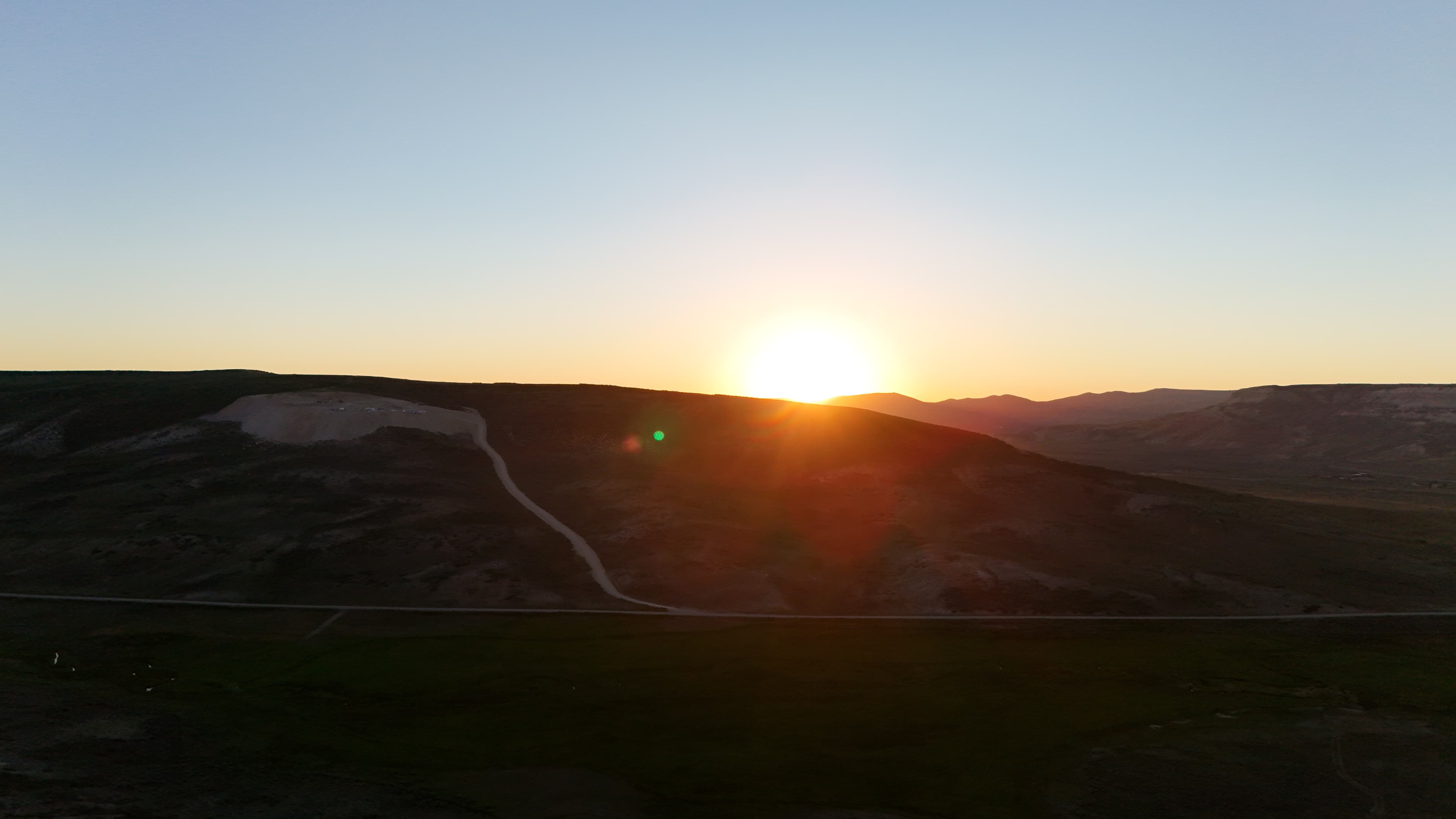 Sunrise over hills with a road and a dug-out area.