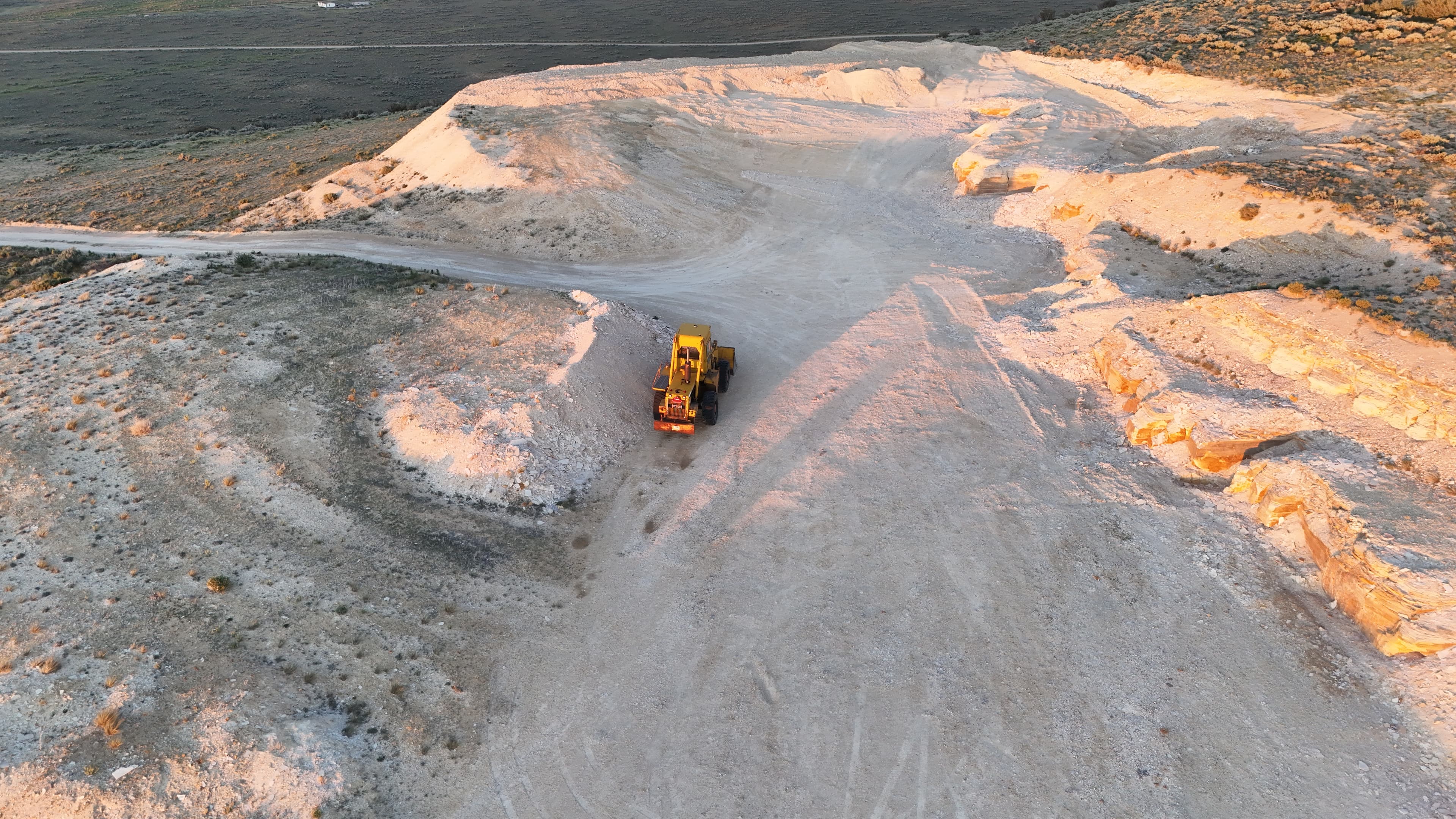 Yellow loader moves dirt on dusty hills at sunset.