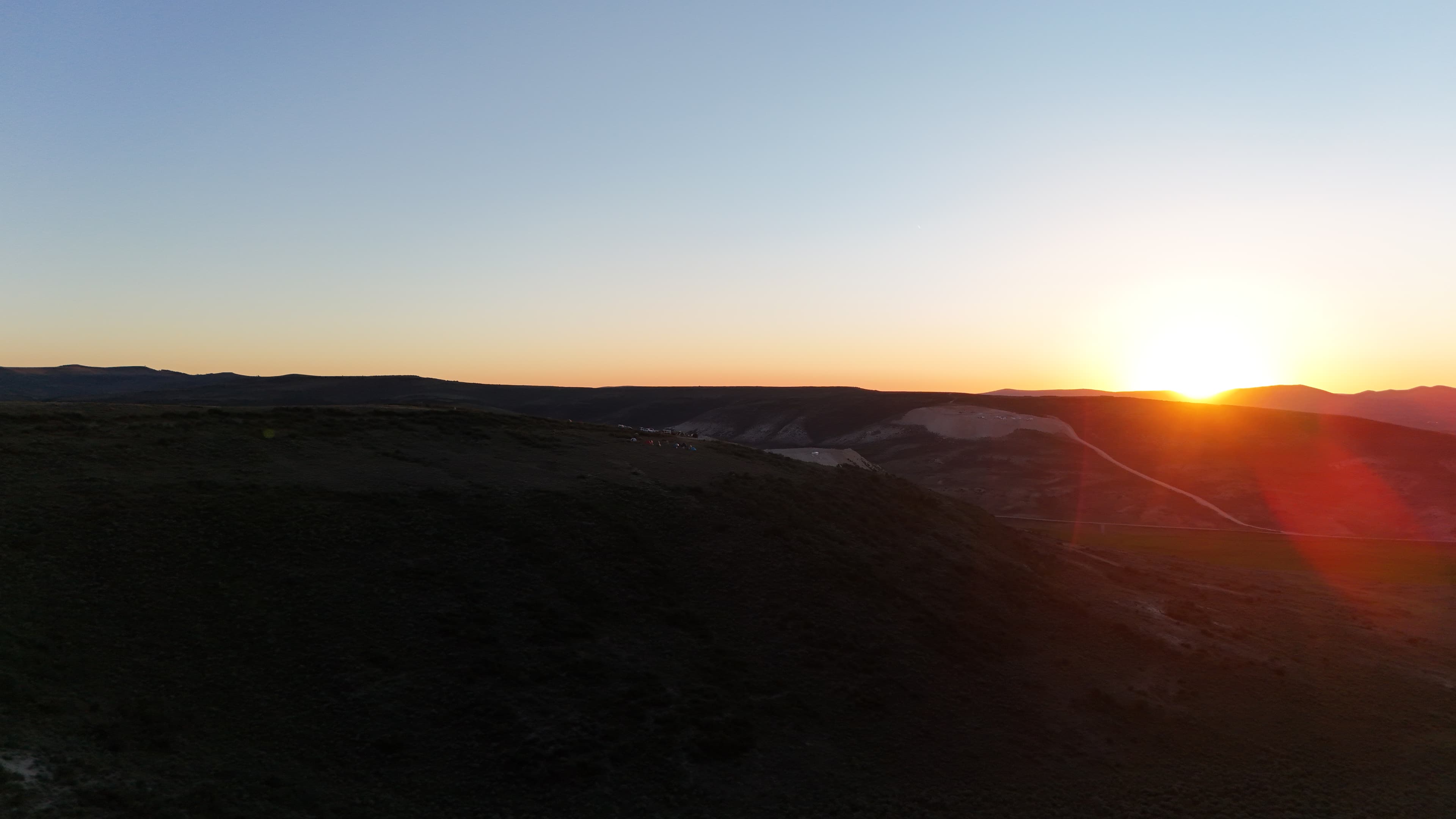 Distant tents and vehicles scattered across the hillside at sunrise.