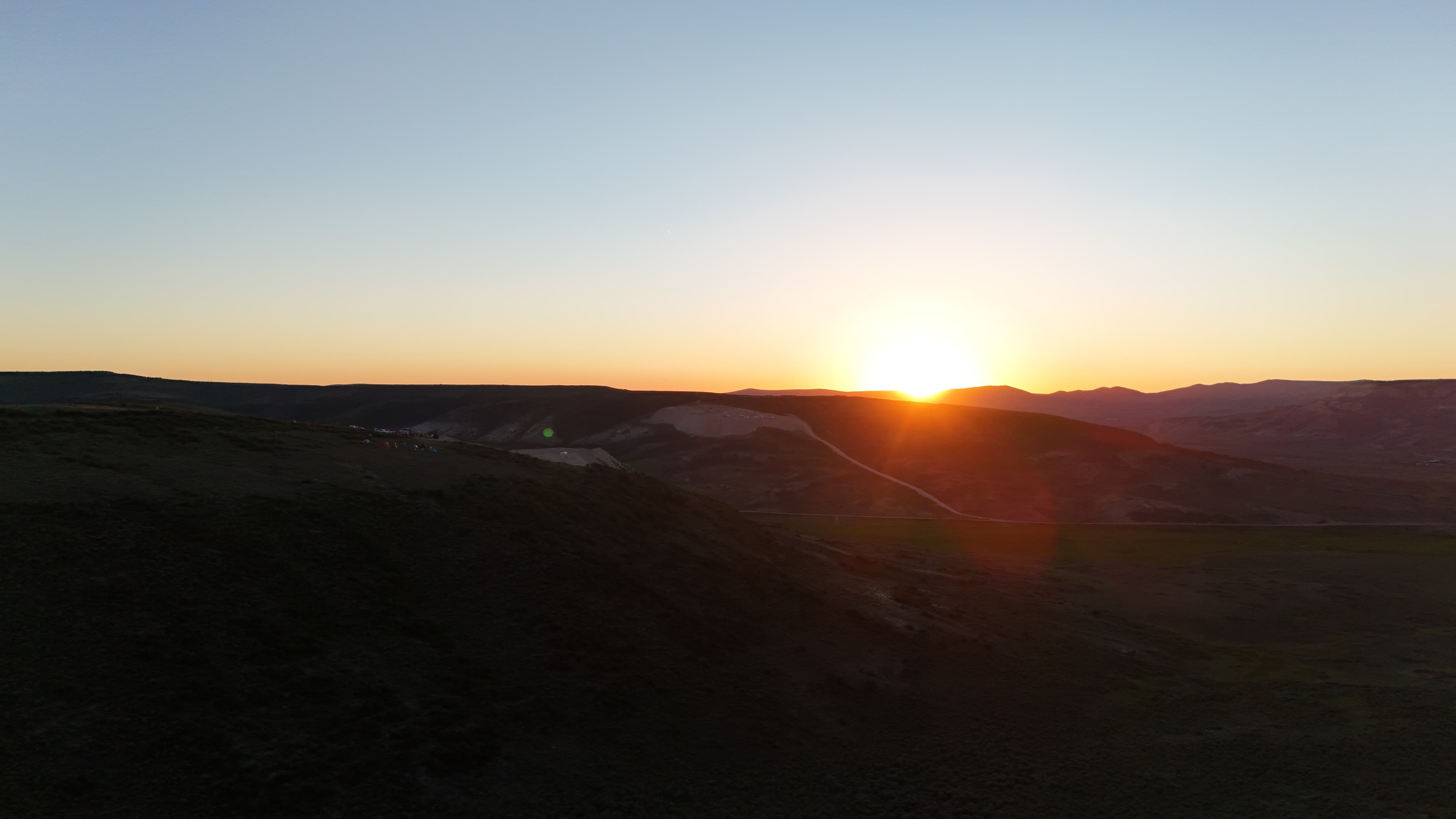 Sunrise over dig site with camp tents visible on the ridge.