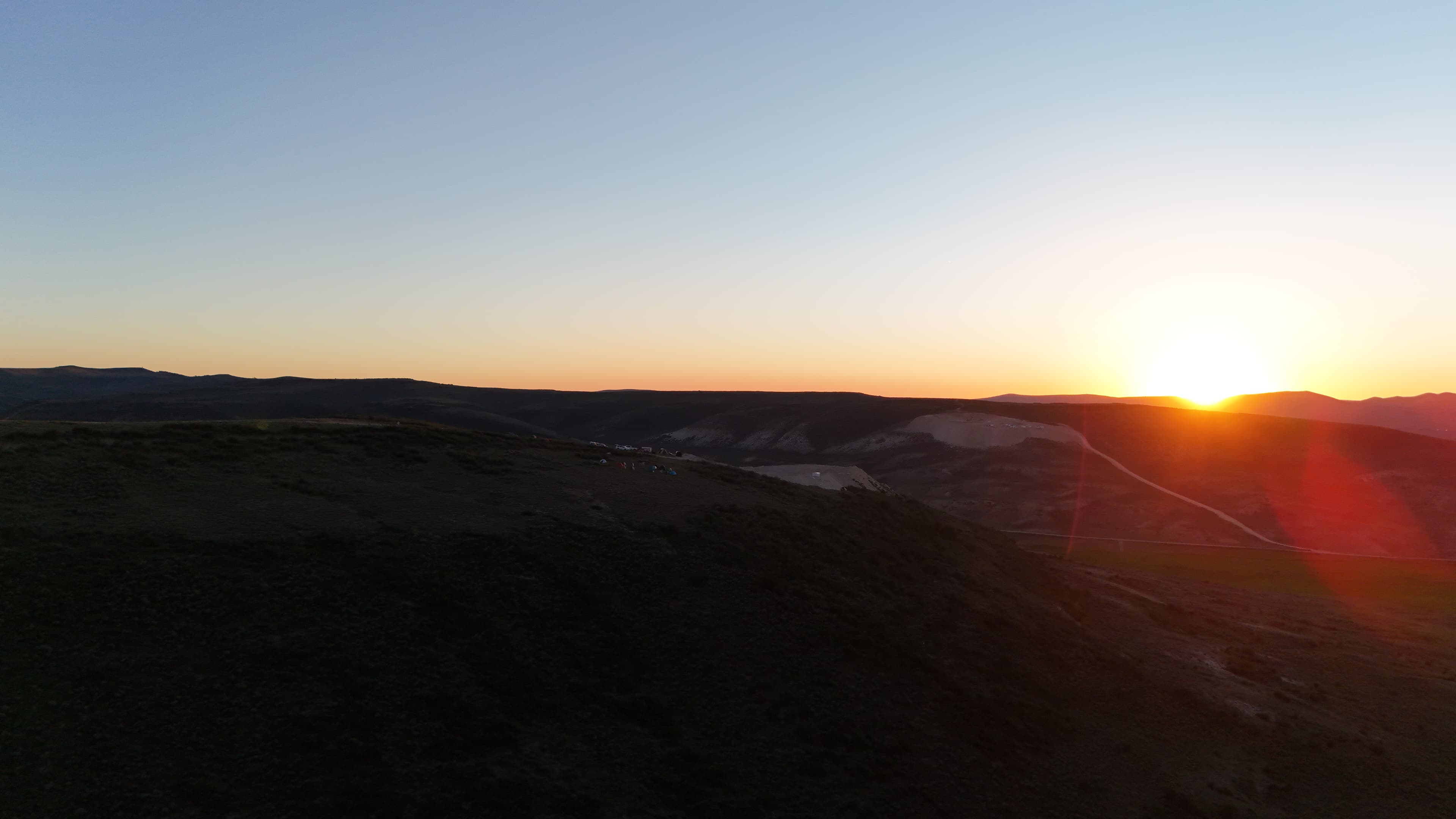Camp tents and vehicles spread across the hill at sunset.