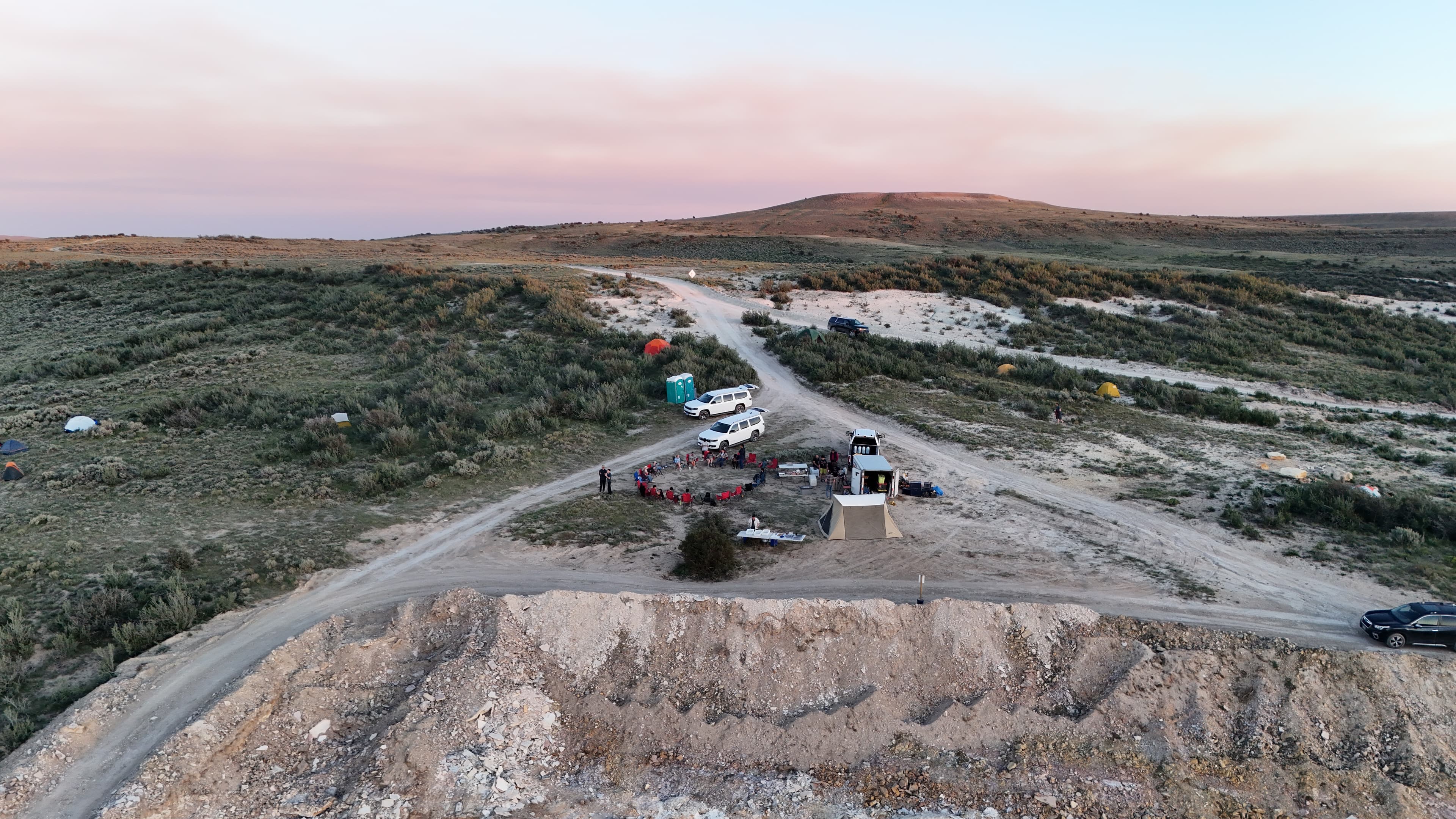 Camp and vehicles are set up on dusty roads under a pale sky.
