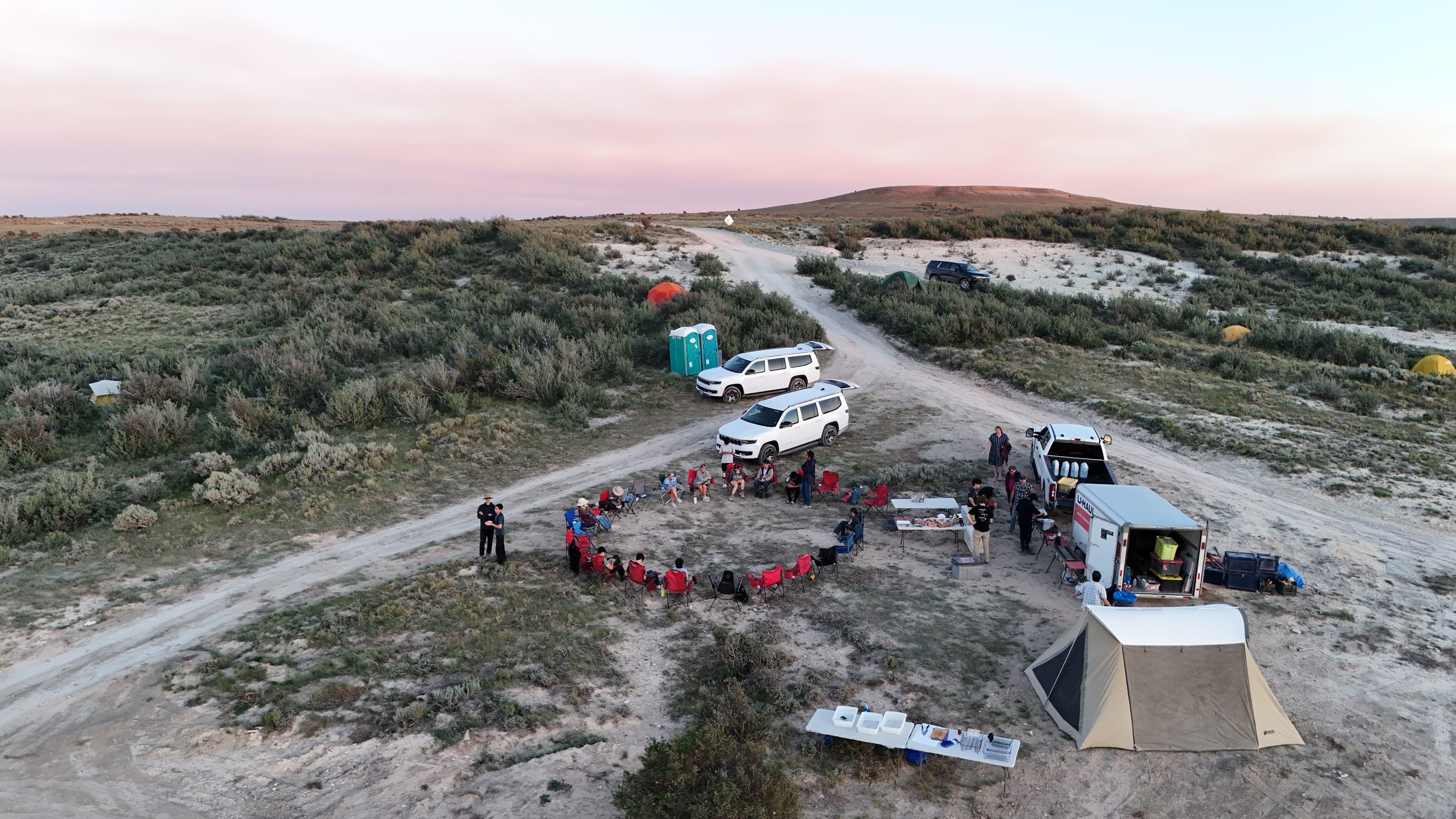 Campers gather near trucks under a pale Wyoming sky at dusk.