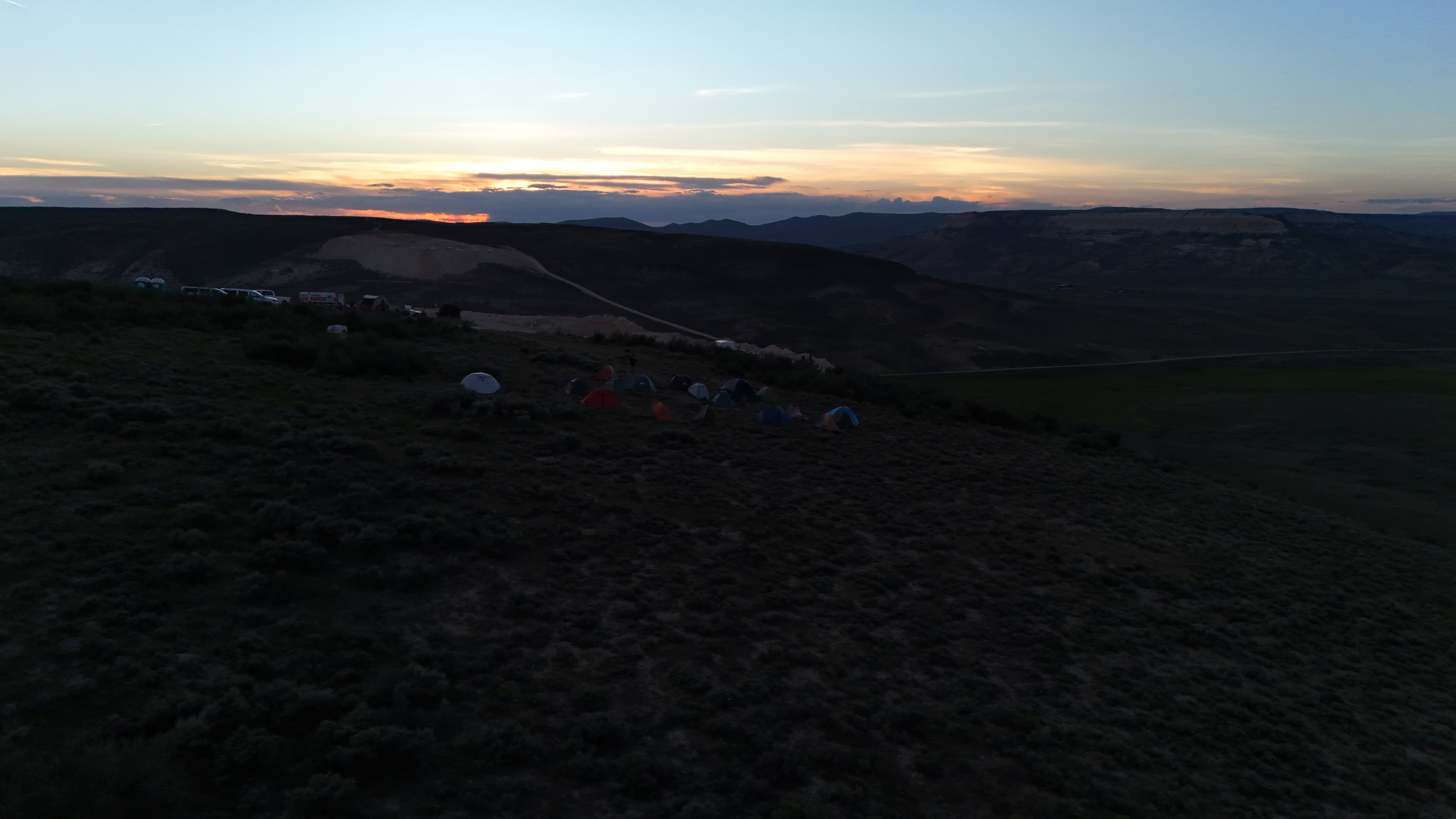 Camp tents spread out on a hillside at sunset.