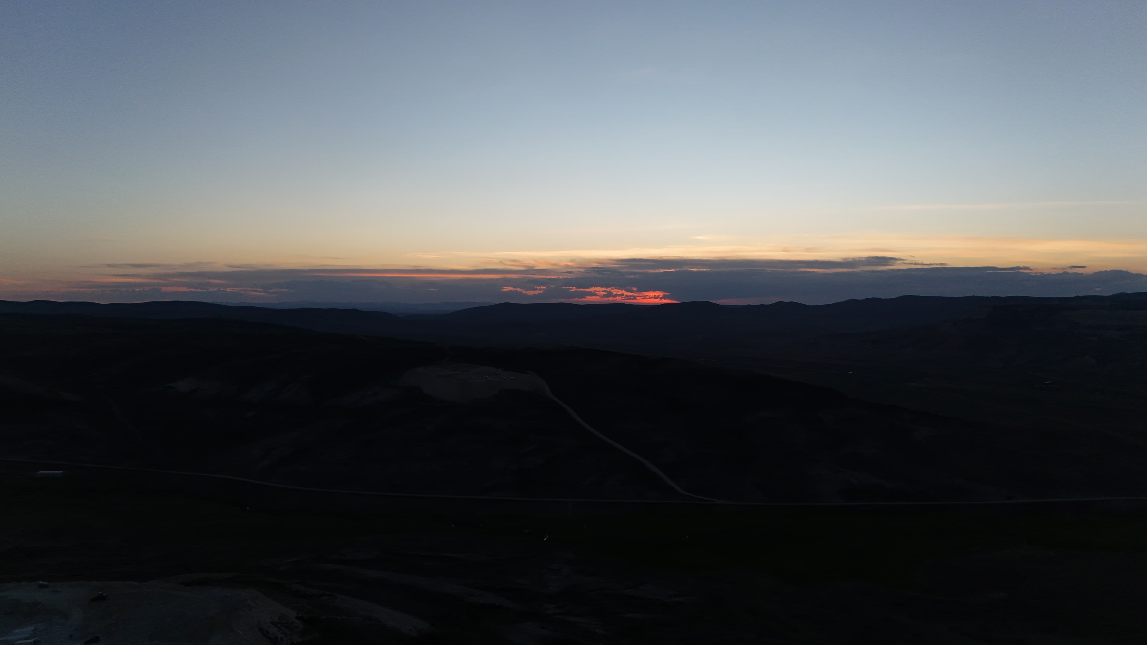 Sunset over hills above a dark quarry site.