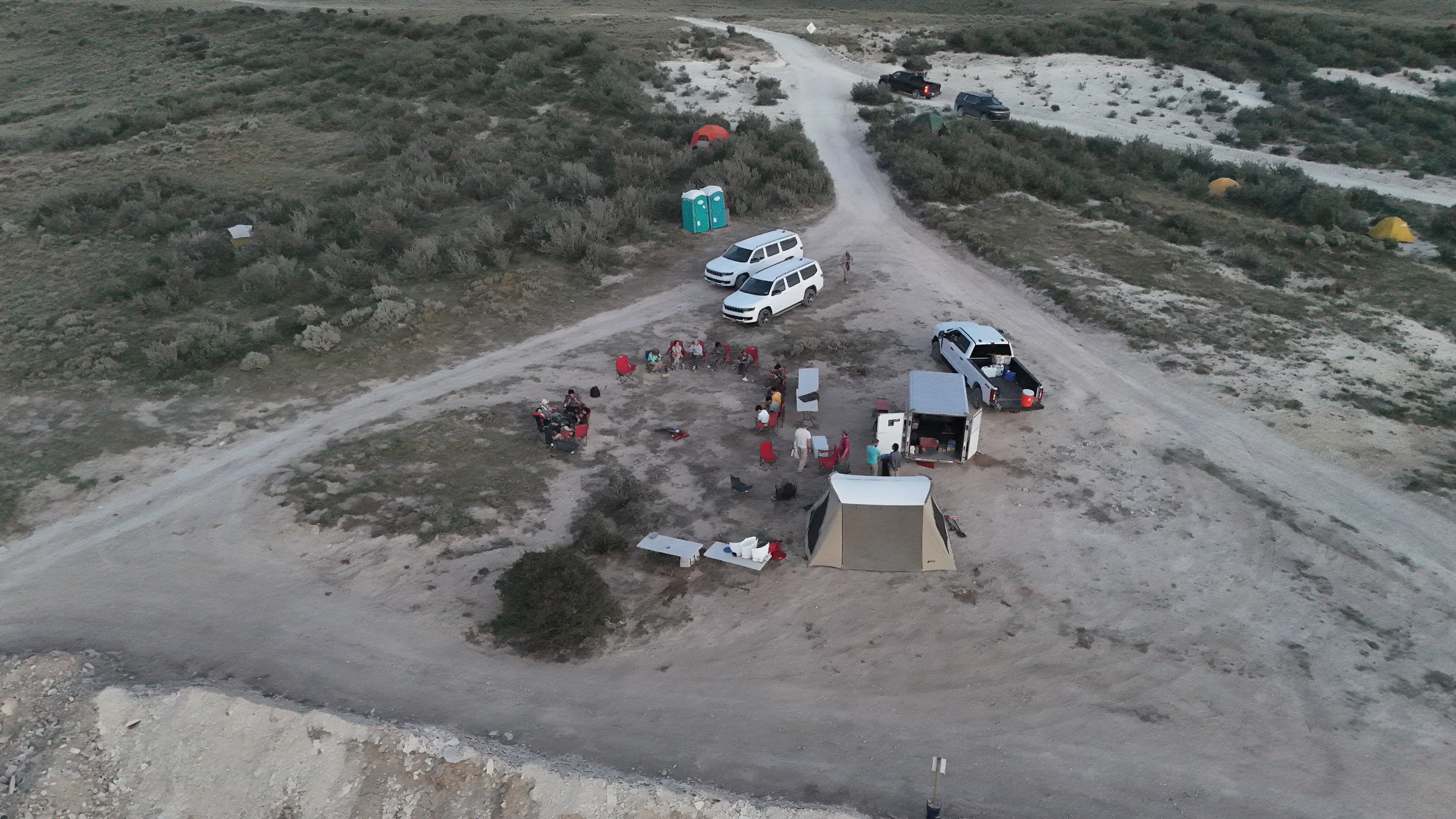 Camp is set up with tents, vehicles, and people by the dirt road.