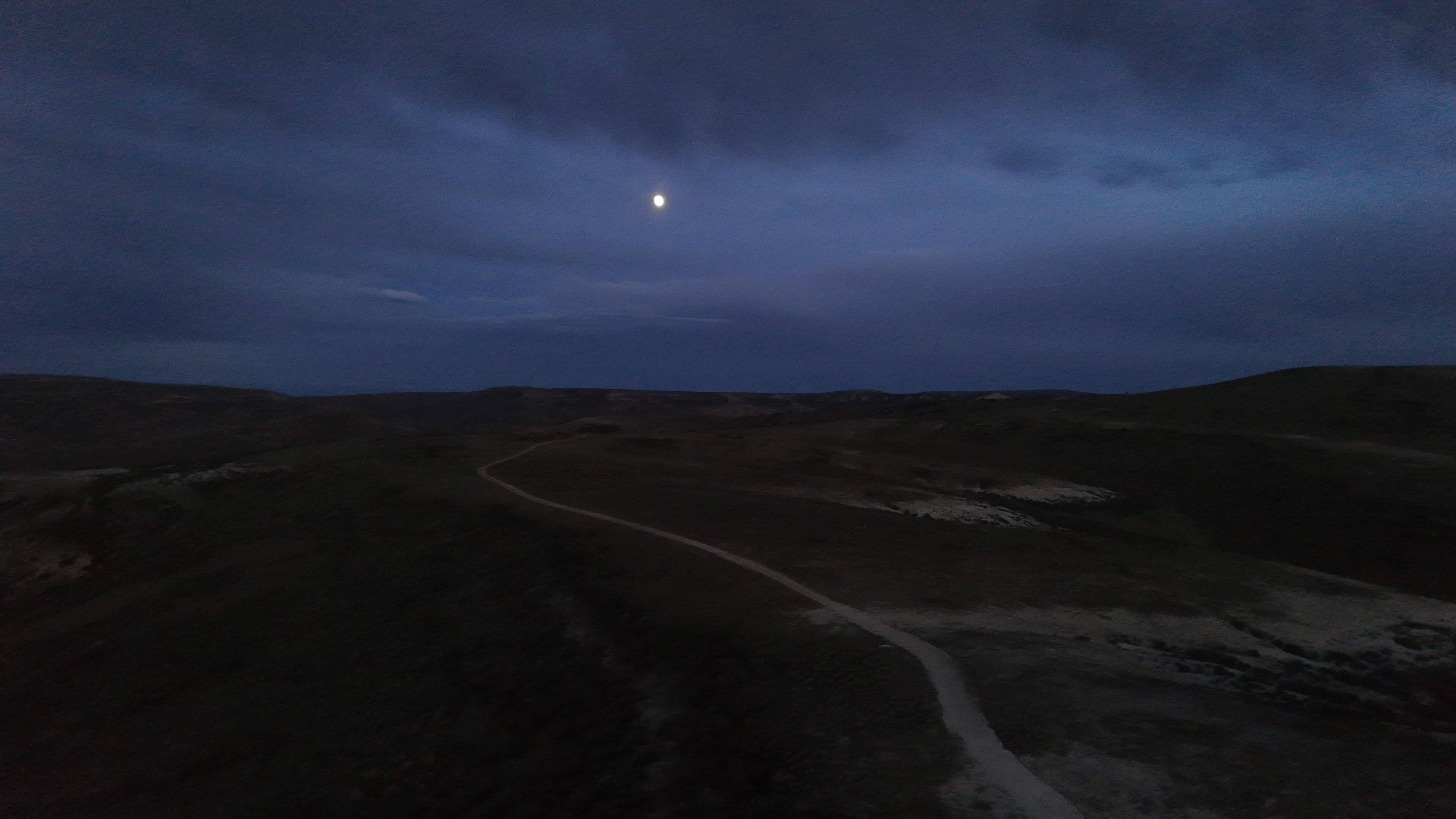 Moonlight over rolling hills and a dirt road at dusk.