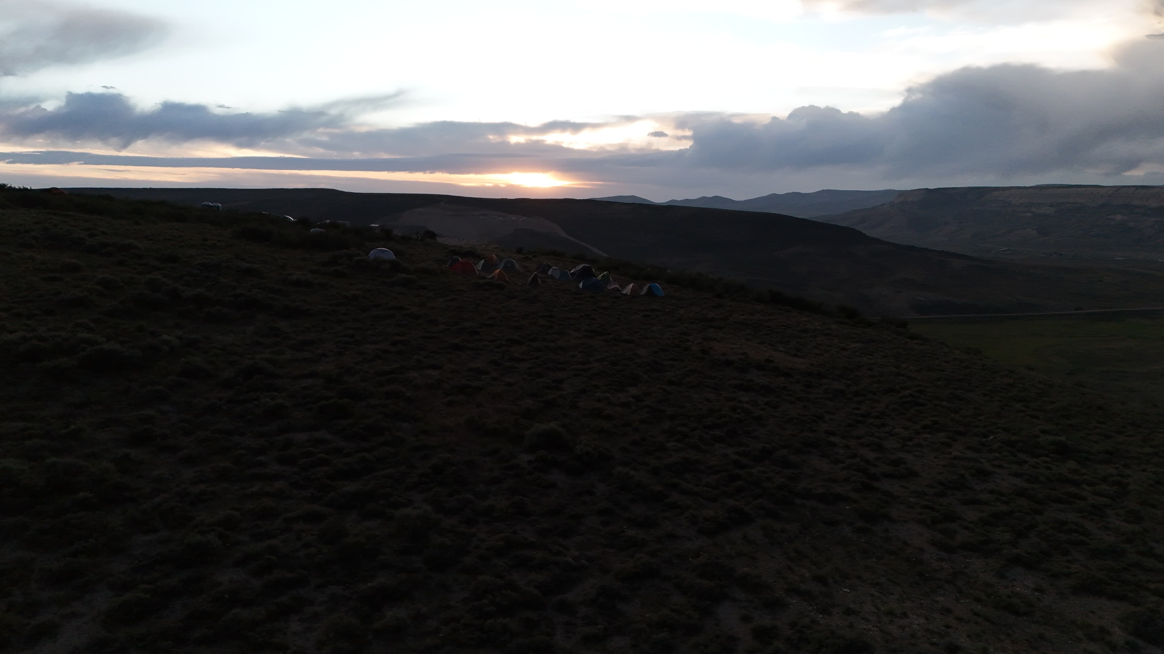 Tents dot the hillside under a cloudy Wyoming sunset.