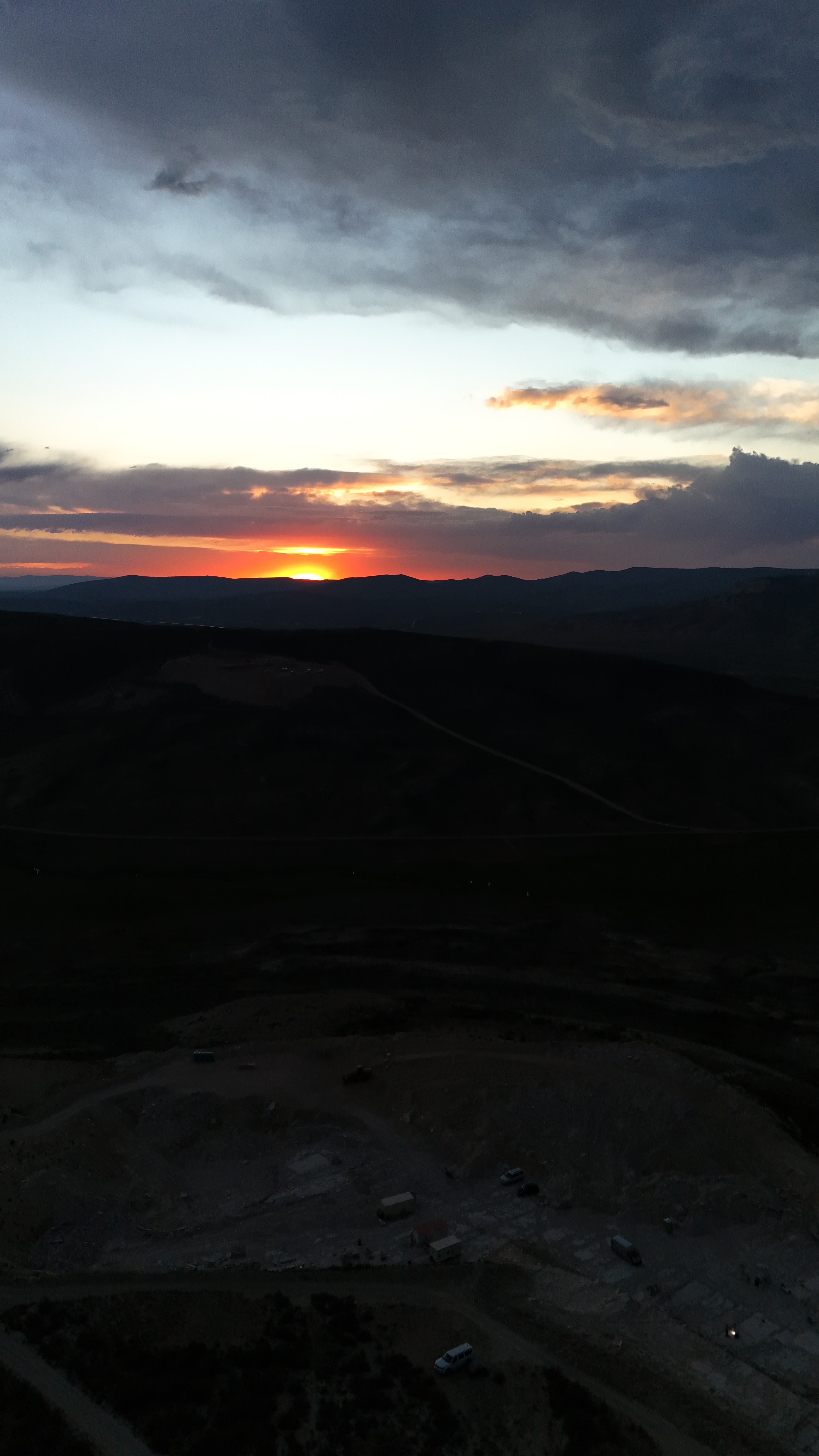 Camp trucks sit by hills at a fiery sunset.