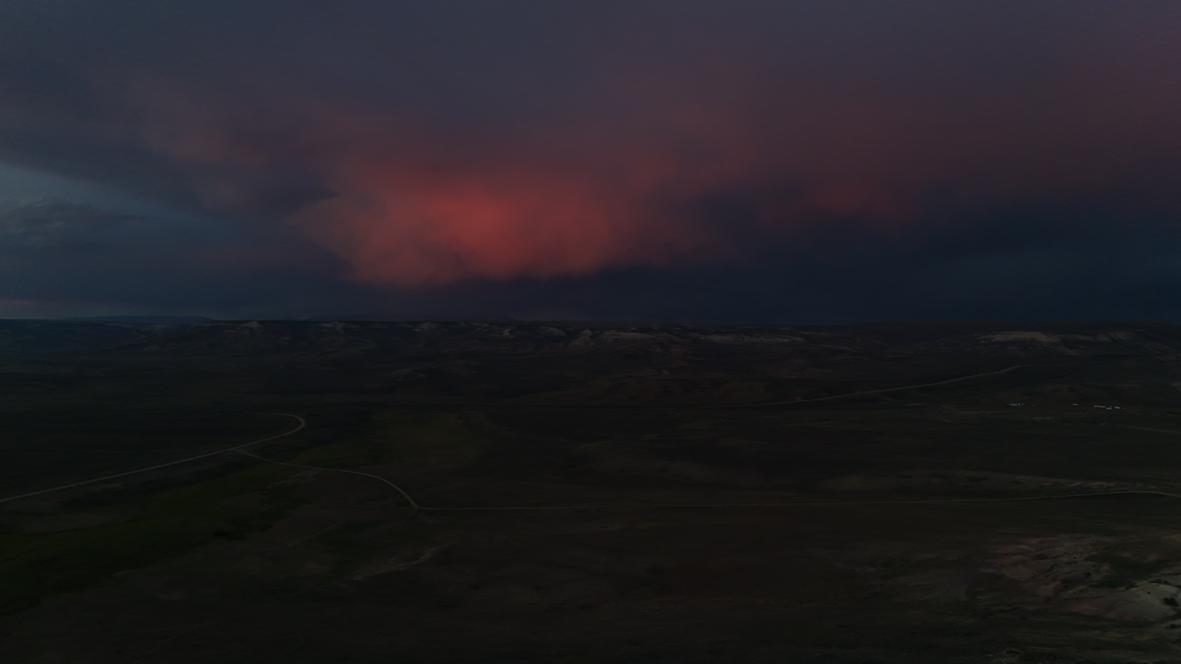 Dark stormy clouds with a bright red glow over the hills.