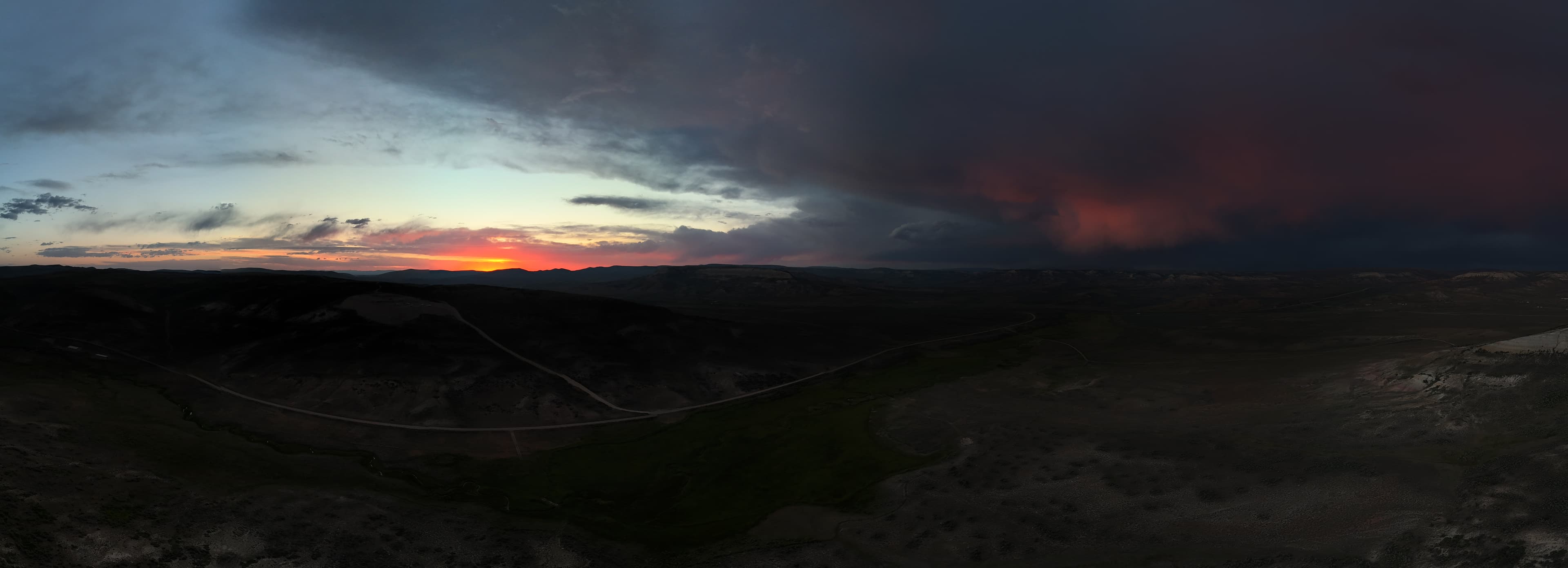 Storm clouds gather over dark hills at sunset.