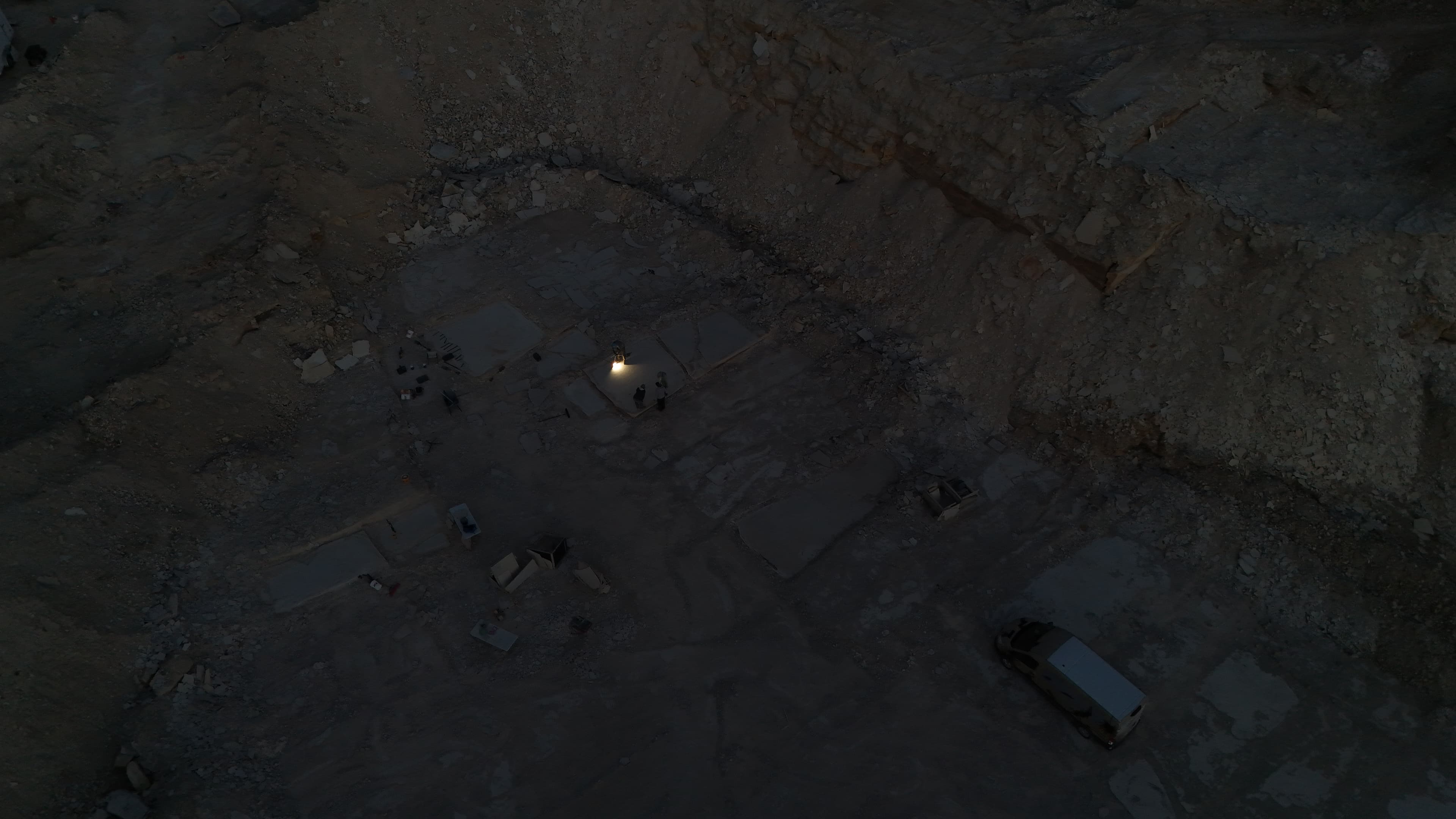 People working under lights in a quarry at dusk.