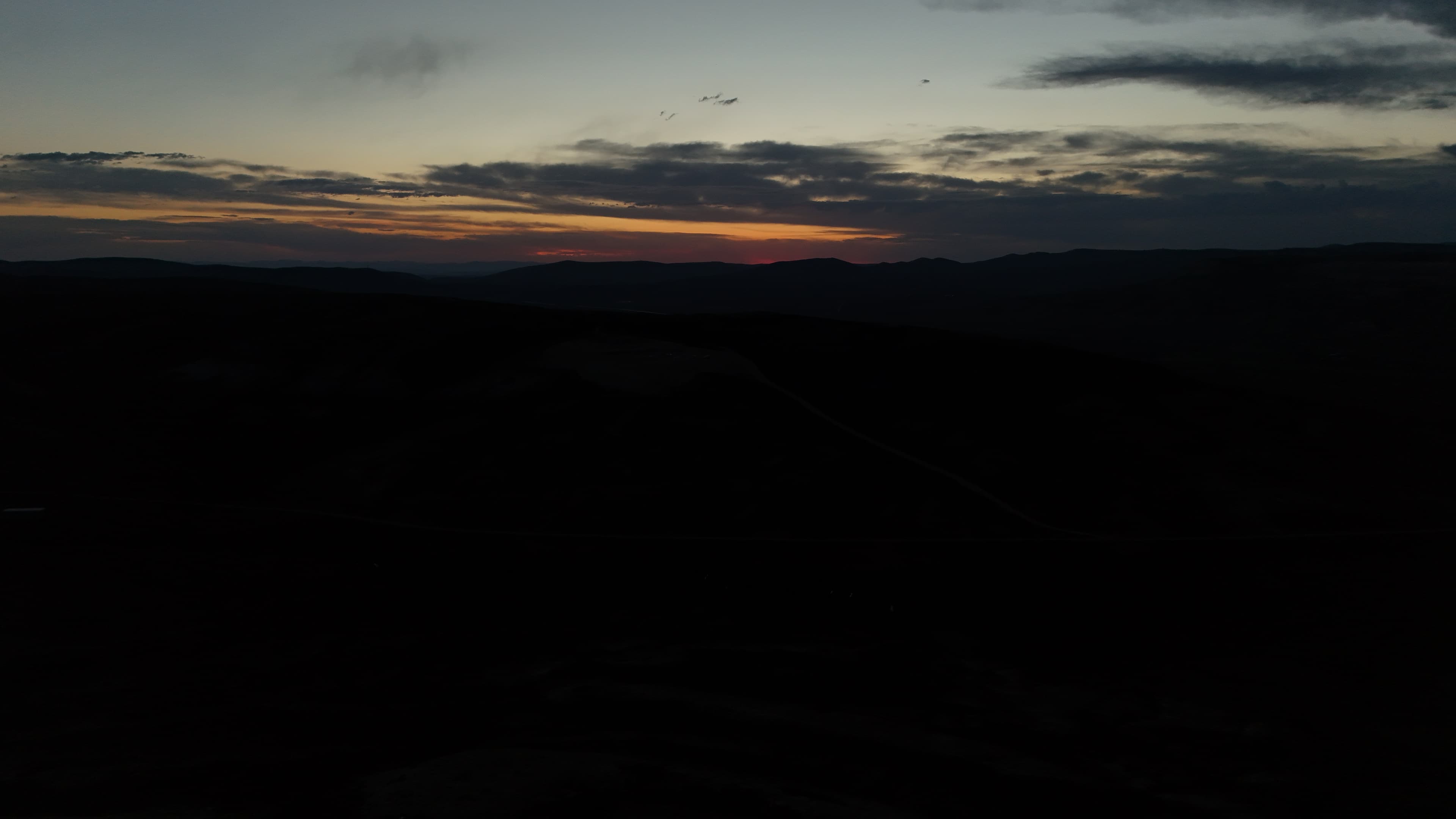 Dark hills under a pale orange and gray sky at dusk.